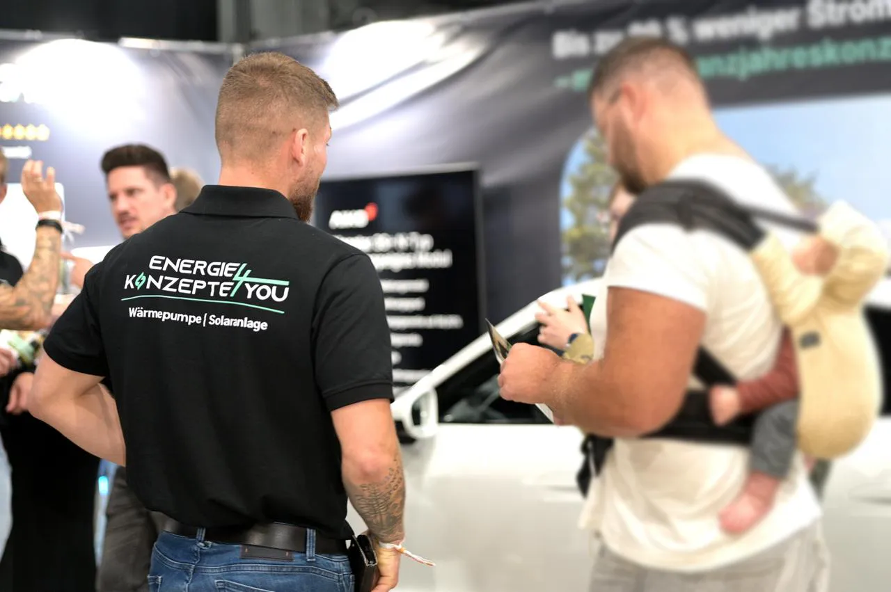 EK4YOU Mitarbeiter im Gespräch mit einem Besucher auf einer Messe, im Hintergrund der Messestand zu Wärmepumpen und Solaranlagen.
