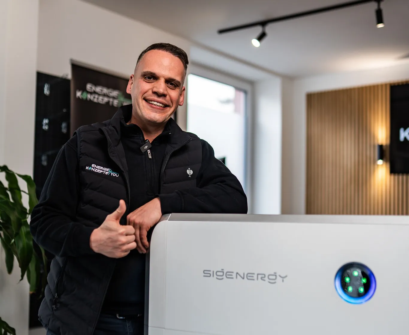 Beratung anfragen - EK4YOU Mitarbeiter präsentiert einen Sigenergy Energiespeicher im Showroom und zeigt den Daumen hoch.